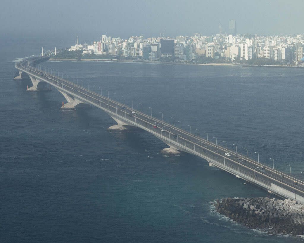 A long bridge passes over the ocean toward a city in the distance.