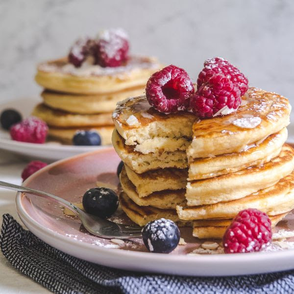 Two stacks of pancakes with raspberries and blueberries on plates
