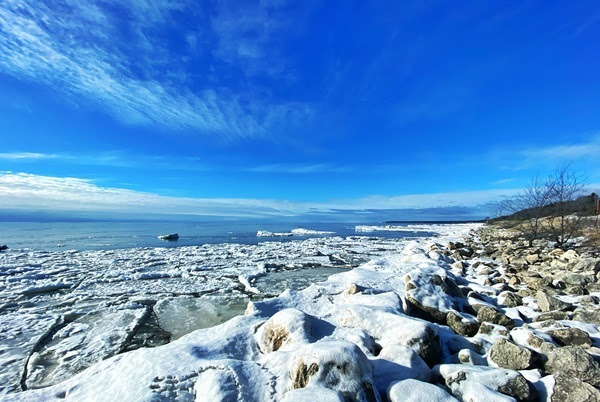 view from Hog Island Point State Forest Campground of snow-covered rocks, icy Lake Michigan shoreline and brilliant blue winter sky