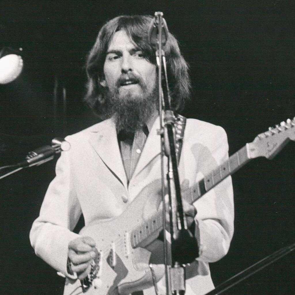 A black-and-white photo of George Harrison of the Beatles, playing guitar.