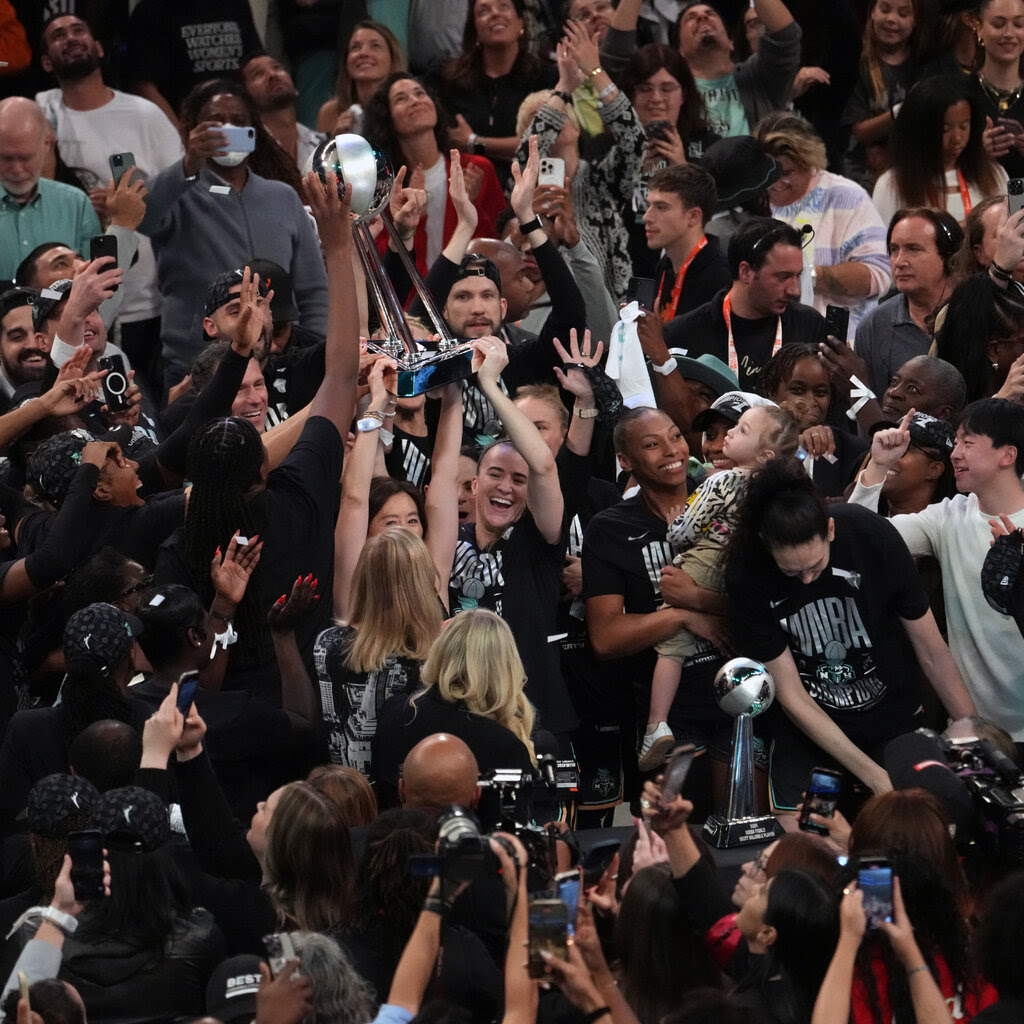 Women hold up a trophy in a crowd.