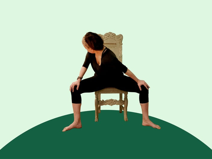 Woman doing chair yoga horse pose on green background.