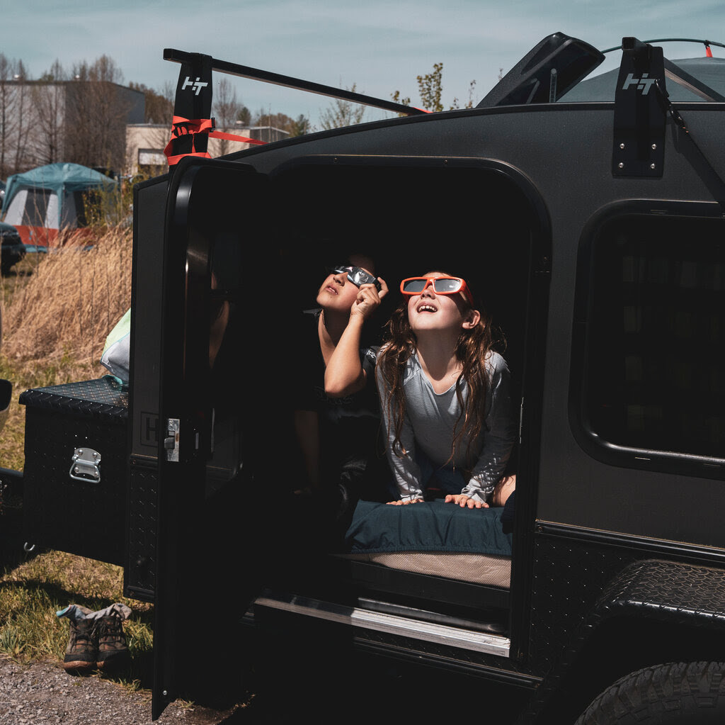 Two young girls stare up at the sky from inside a camper van. 