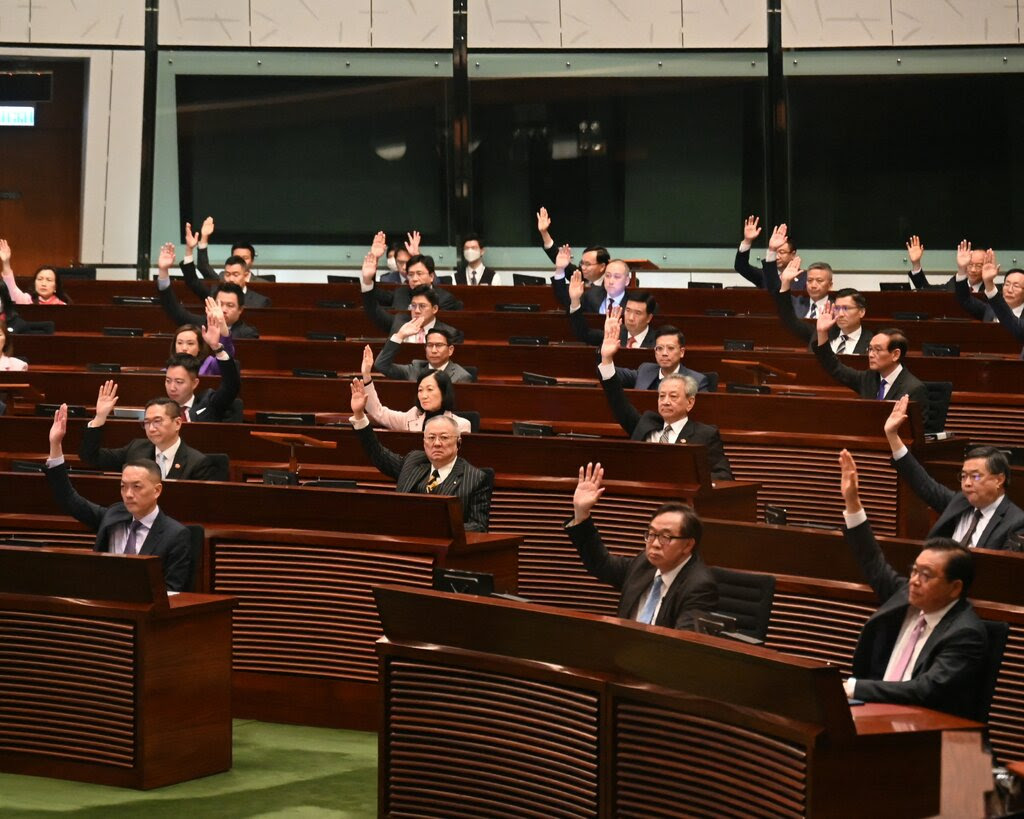 Lawmakers sitting in rows inside Hong Kong’s legislature vote by raising their hands.
