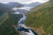 Aerial view of a river valley with evergreen trees and mild cloud cover.