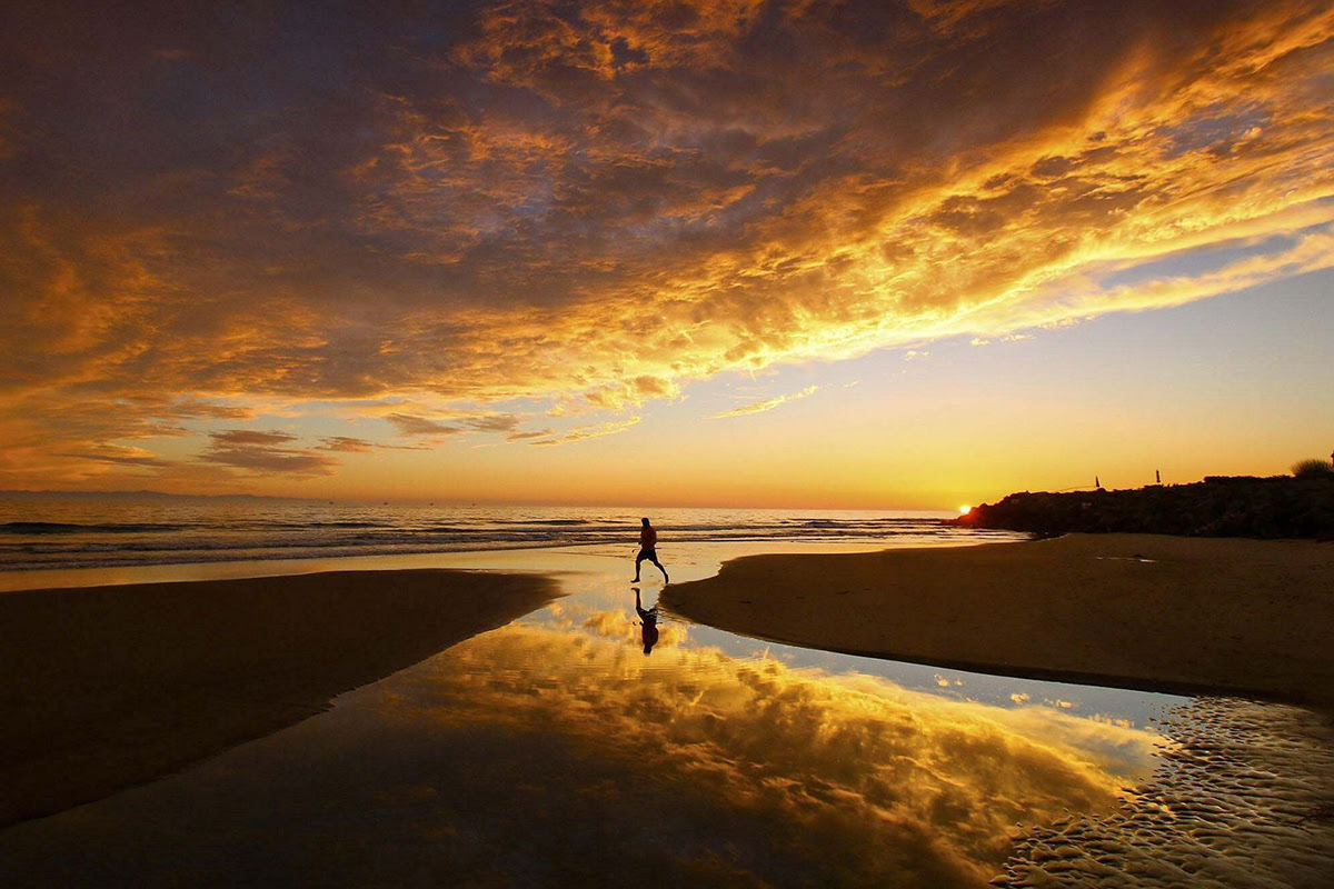 A person jumps across water at a sunset coastal scene. © John Nordstrand © undefined