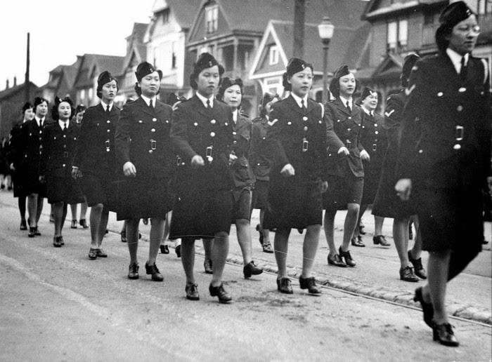 A black and white photograph of an Ambulance Corps made up of Chinese Canadian women marching through Vancouver during the second world war