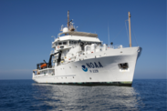 Side view of a white NOAA Ship on open water on a clear, sunny day