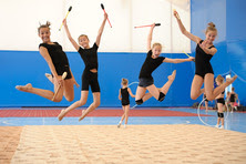 a group of young girls are caught jumping mid air, smiling, they are in a gymnasium