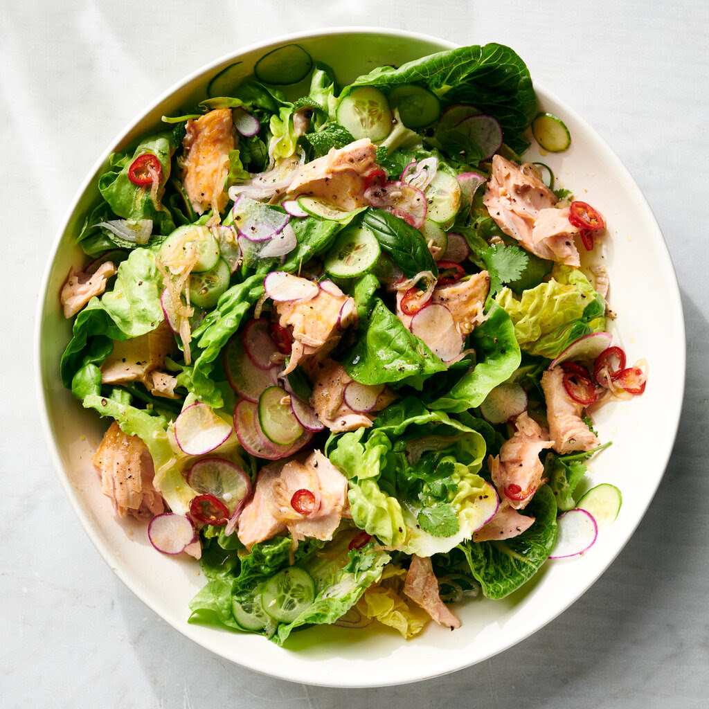 Pieces of salmon and slices of cucumber, chili and radishes sit on a bed of salad in a white dish.