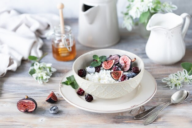 Cottage cheese with figs, berries, honey. Cup of coffee and coffee pot. Breakfast. Wooden table.