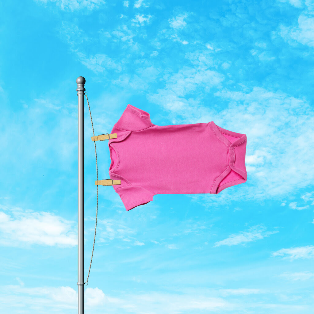 A photo illustration shows a pink onesie attached to a flagpole against a blue sky background.