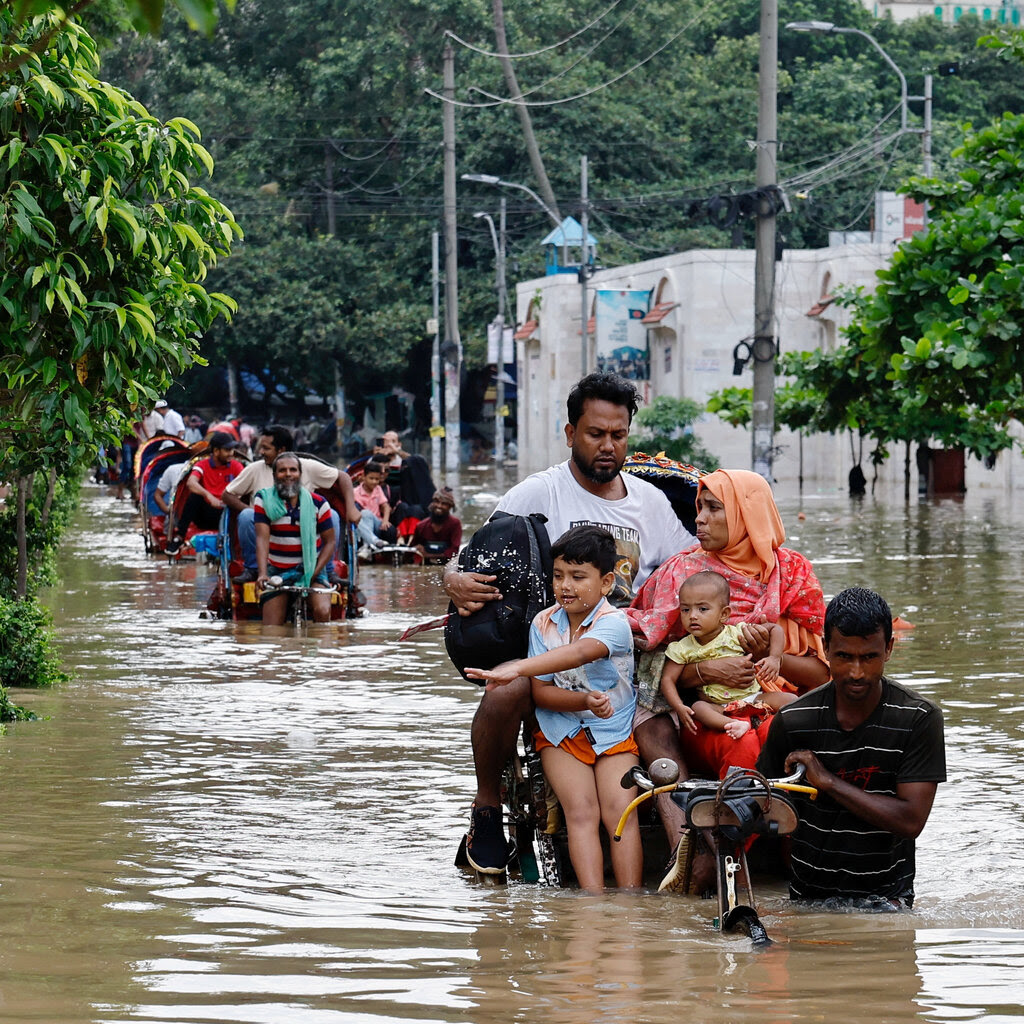 A family sits on a rickshaw trudging through brown floodwater.