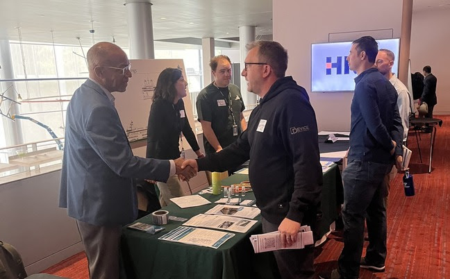 Three people behind a table at a conference with three visitors, with two of them shaking hands