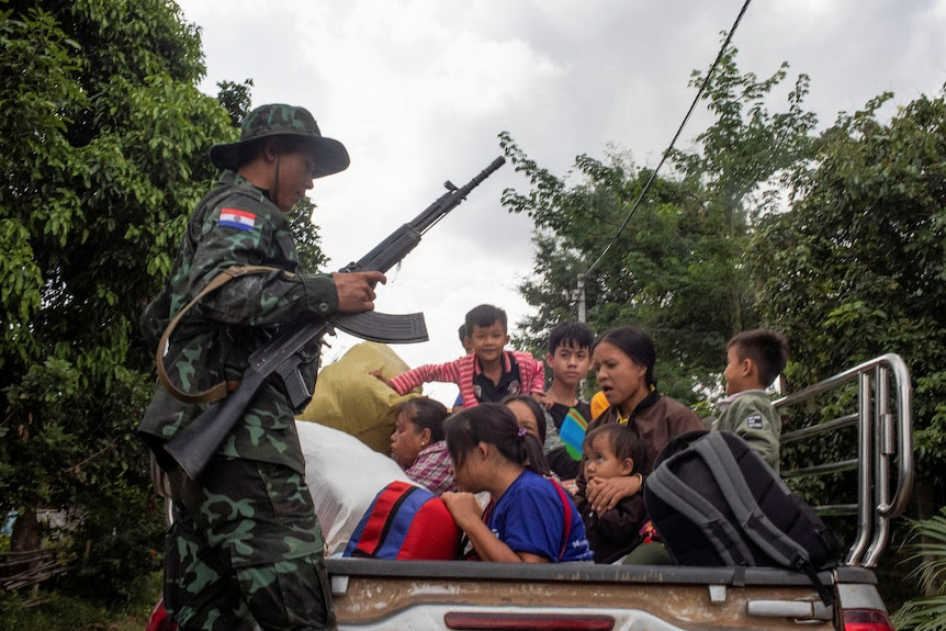 A soldier holding a run looks over a mother and children sitting in the back of a truck