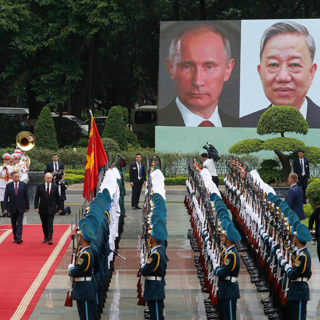 Vladimir Putin, second from left, walking on a red carpet while inspecting rows of uniformed military officers at attention. 