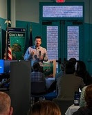 A person speaking to a group of in front of a presentation screen