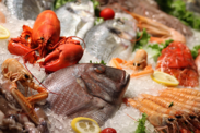 Assorted fresh seafood on ice, including a lobster, whole fish, shrimp, and crab, garnished with lemon slices and cherry tomatoes.