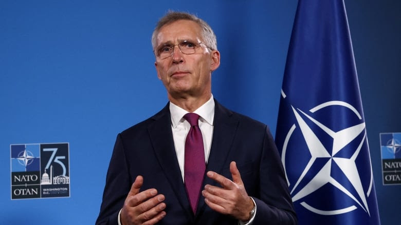 A man with glasses in a suit and tie speaks and gestures at a podium.