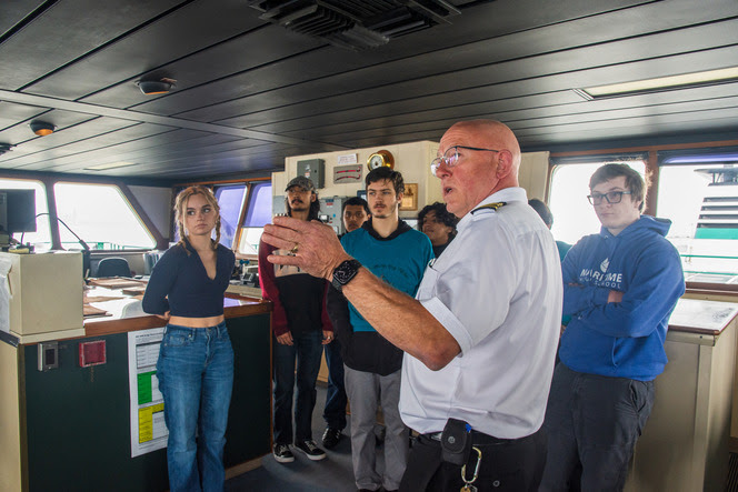 Ferry crew member in white uniform speaking to students in the wheelhouse 