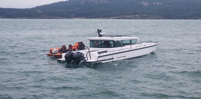 Rescue boat alongside a small vessel with ferry crews assisting people on the vessel onto the rescue boat