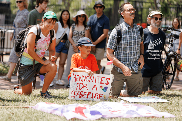 A woman, boy, and two men kneel in the grass. The child holds a sign that says 