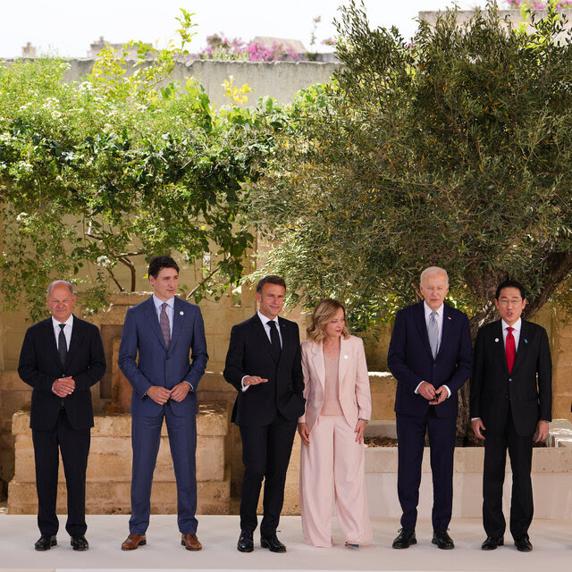 World political leaders including U.S. President Joe Biden pose in a single line for a photo in front of foliage. 