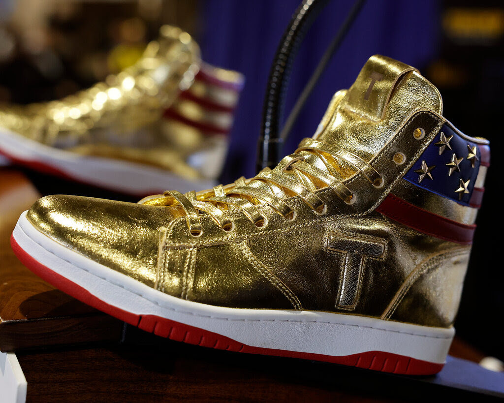 A pair of golden sneakers that feature an American flag design around the back of the ankle and a “T” stitched into the side.