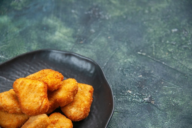 Close up shot of tasty chicken nuggets in black plate on dark surface with free space