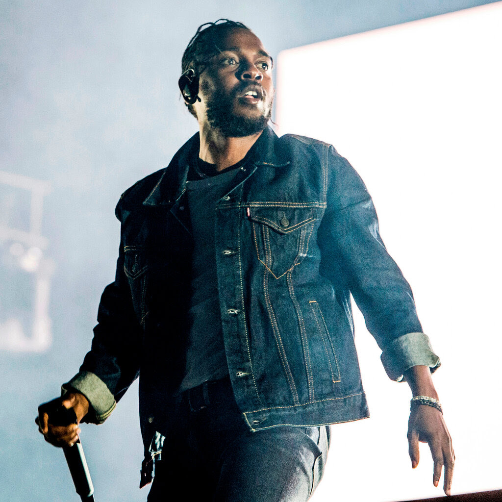 Kendrick Lamar, in a jeans jacket, holds a microphone in one hand onstage.