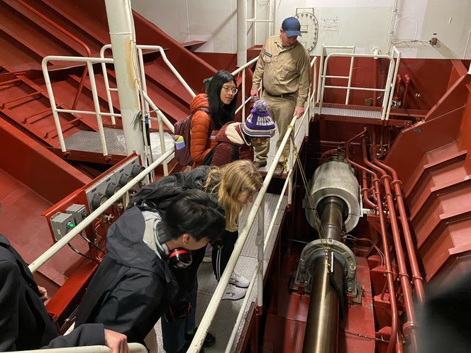 Several people look at the engine of a ferry