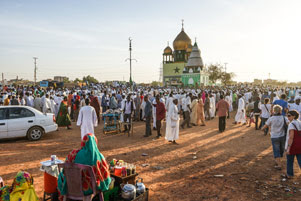 A large group of people are gathered around a small mosque.