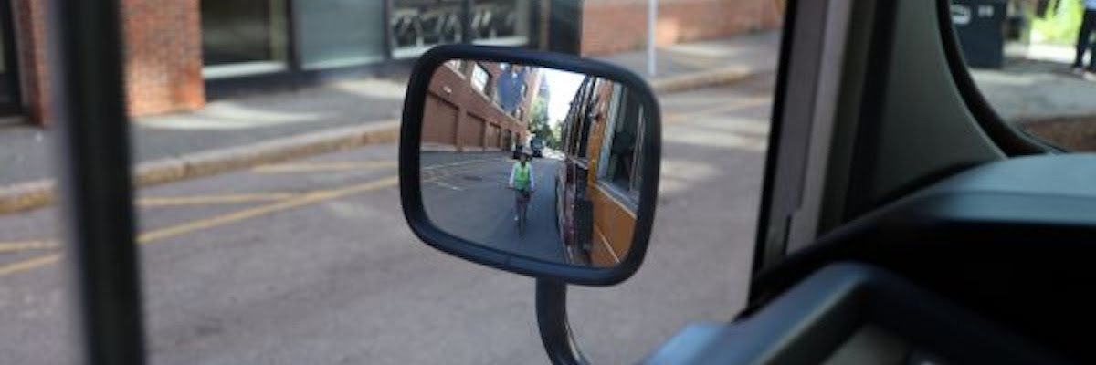 a biker wearing a reflective vest as seen in
the side-view mirror of a bus