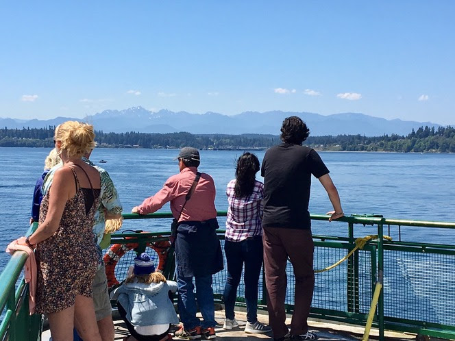 Several people on the outdoor deck of a ferry on a sunny day