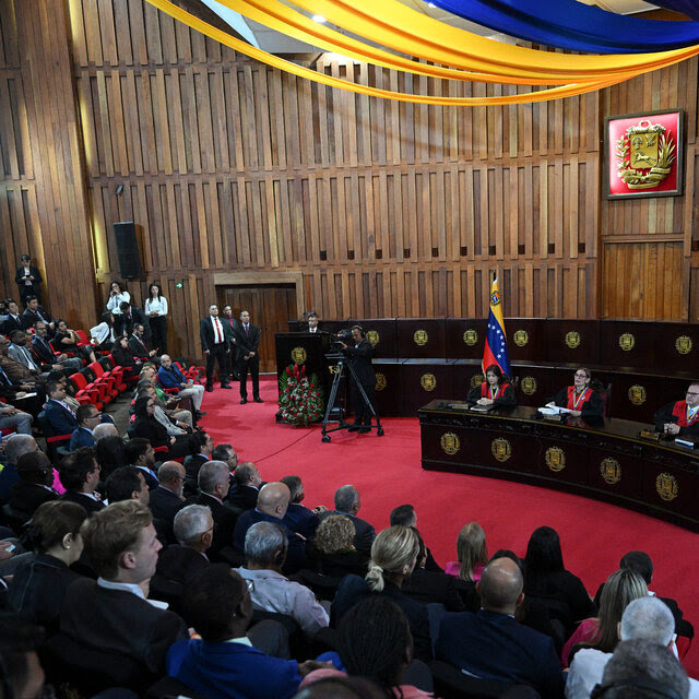 Three judges sit at a desk with bunting in the colors of the Venezuelan flag behind and above them.