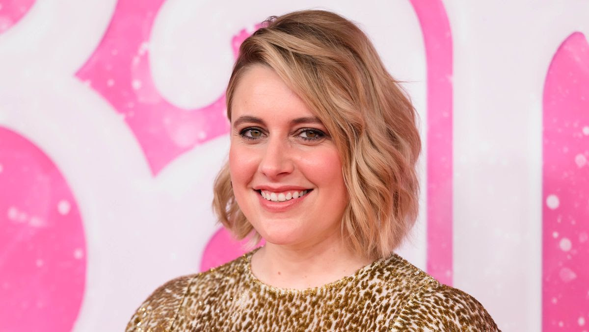 The film-maker Greta Gerwig smiles in front of a pink Barbie background