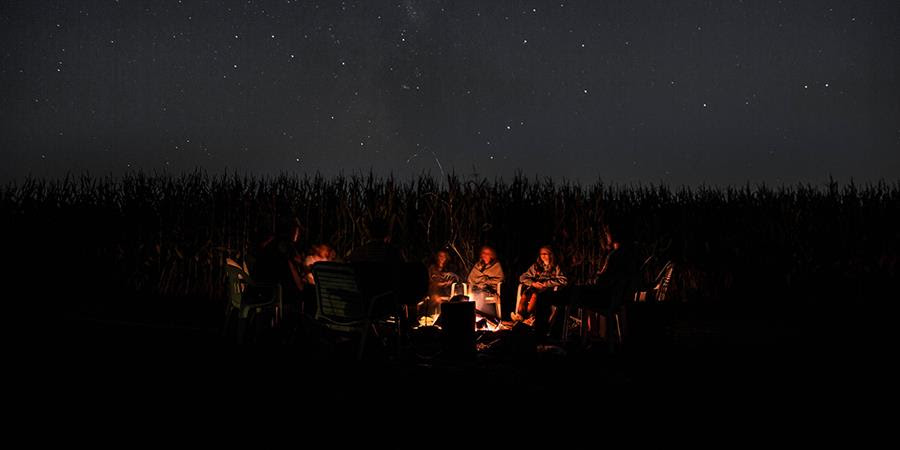 A photo shows people around a campfire under a dark night sky.