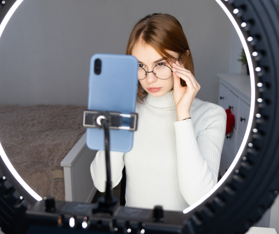 リングライトの中にiPhoneをつけて自撮りしているメガネをかけた若い女性