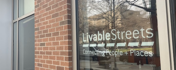 The outside of the LivableStreets office,

showing the front window with the livablestreets logo in white and

reflections of the street and sidewalk outside