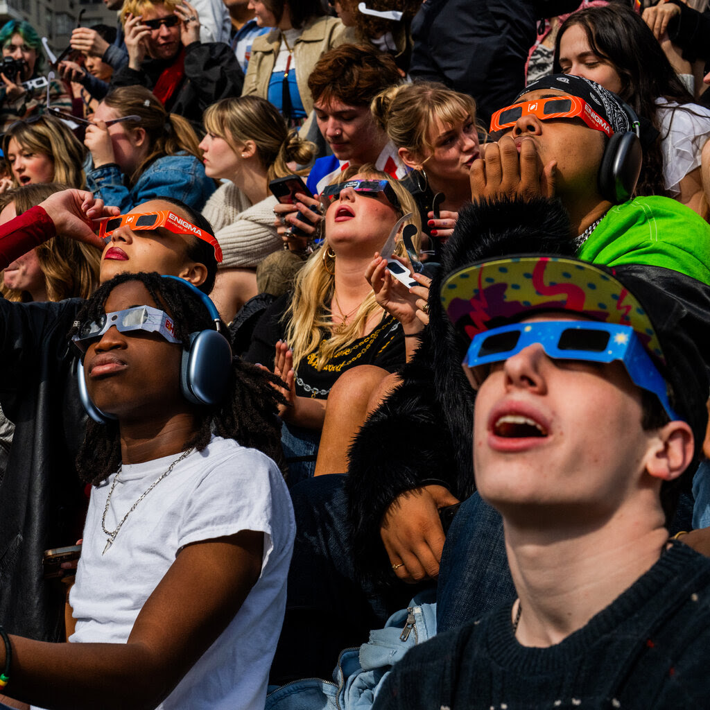 A group of people seated and looking up with eclipse glasses on.