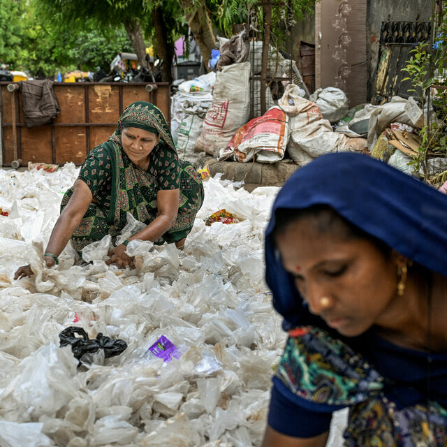 Two women working to sift through a pile of garbage along a city street.