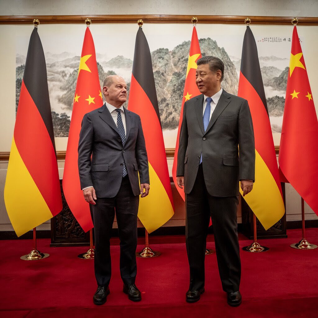Chancellor Olaf Scholz of Germany and Xi Jinping, China’s leader, both in dark suits, stand on a red carpet in front of large Chinese and German flags.