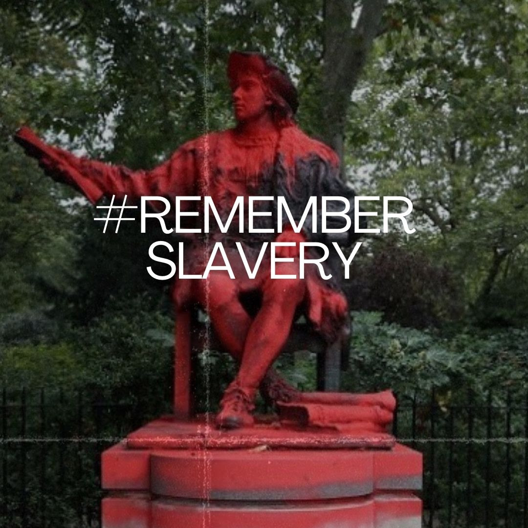 The hashtag 'Remember Slavery' is written over an image of a statue of a seated man holding a scroll, covered in red paint. Behind the statue are railings and luxuriant greenery.