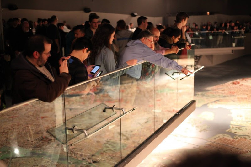 Visitors crowd the walkway surrounding the Panorama; the large scale model of the city below them is visible in the reflection on the glass railing.