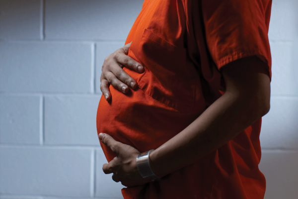 Side view of a pregnant woman in an orange prison shirt holding her baby bump.