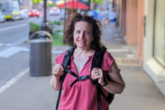 Jennifer Ferdinand stands on a city sidewalk holding the straps of her backpack, smiling at the camera. 