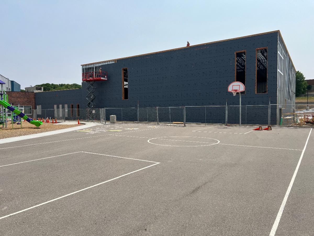 Basketball court next to a building under construction with playground equipment nearby