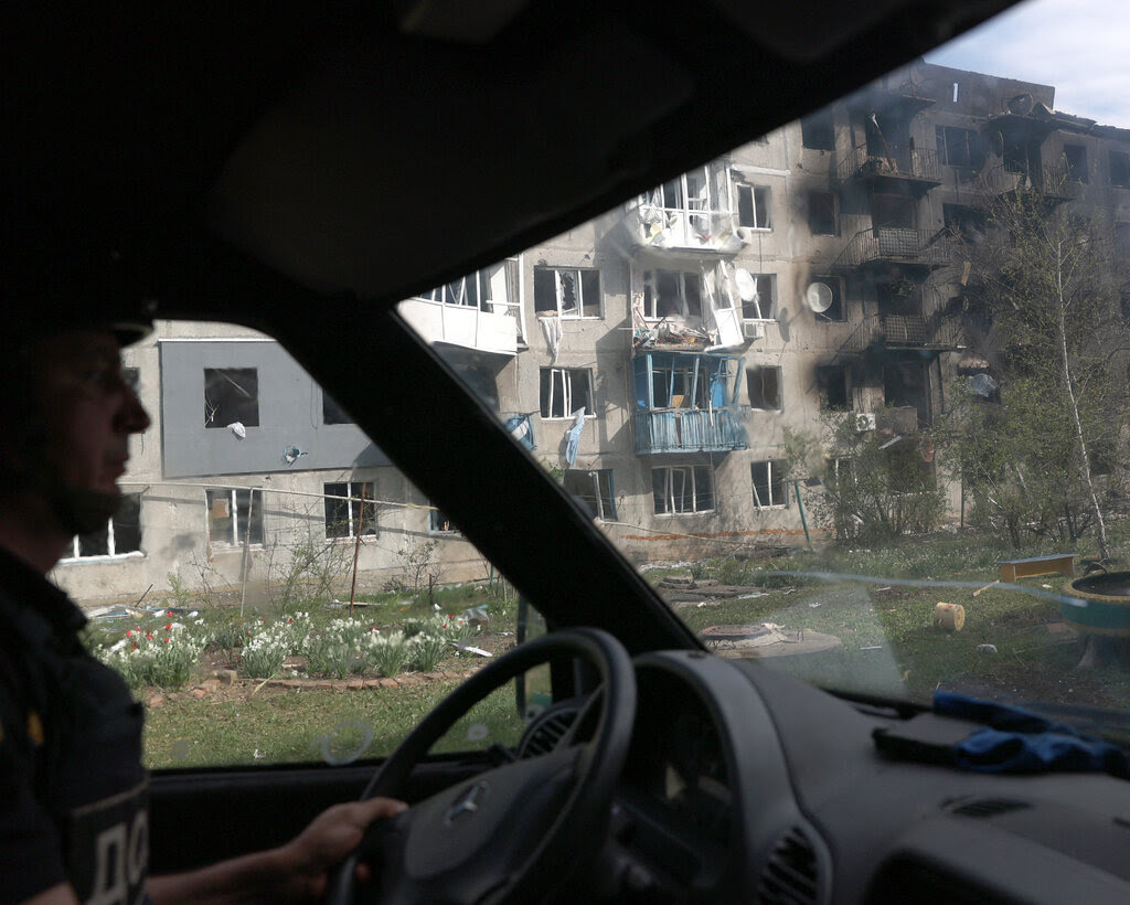 A bombed-out building seen through the windows of a vehicle. 