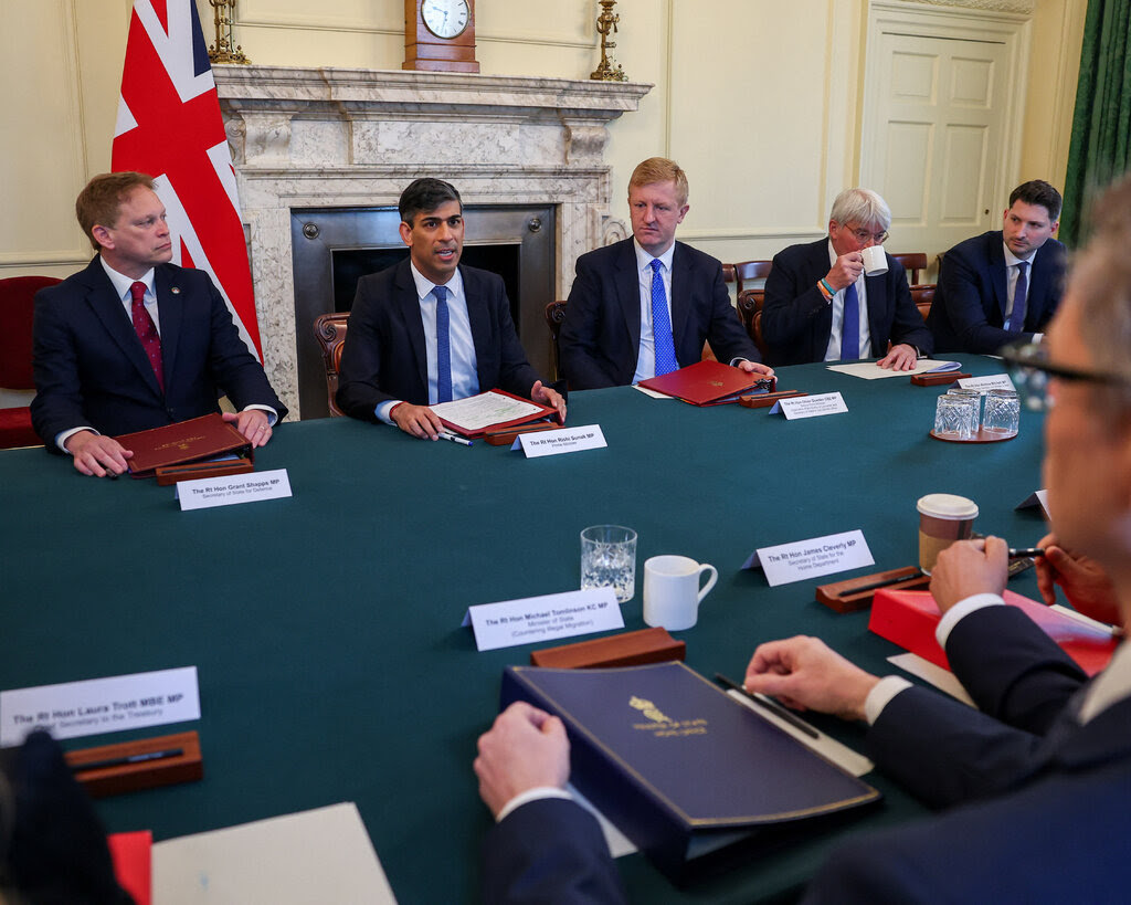 Prime Minister Rishi Sunak of Britain sits at a table flanked by ministers.