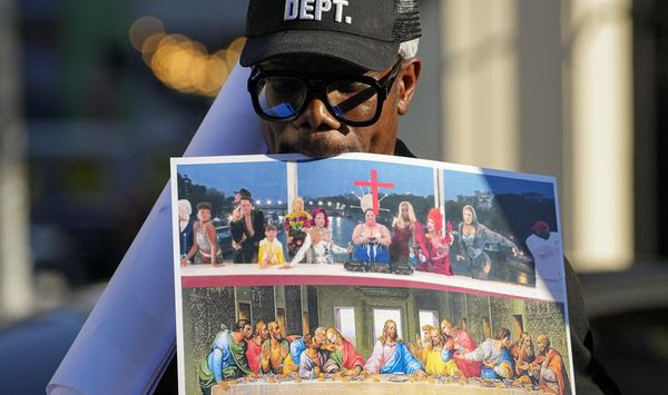 A man holds a piece of paper showing a side-by-side comparison of a scene that took place during the Paris Olympics opening ceremony that seemed to evoke Leonardo da Vinci&#x27;s &quot;The Last Supper,&quot; featuring drag queens and other performers in a configuration reminiscent of Jesus Christ and his apostles, and the original painting, during a protest near the French Embassy in Bucharest, Romania, Sunday, July 28, 2024. Paris Olympics organizers apologized Sunday to anyone who was offended by a tableau that evoked Leonardo da Vinci&#x27;s &quot;The Last Supper&quot; during the glamorous opening ceremony. (AP Photo/Andreea Alexandru)